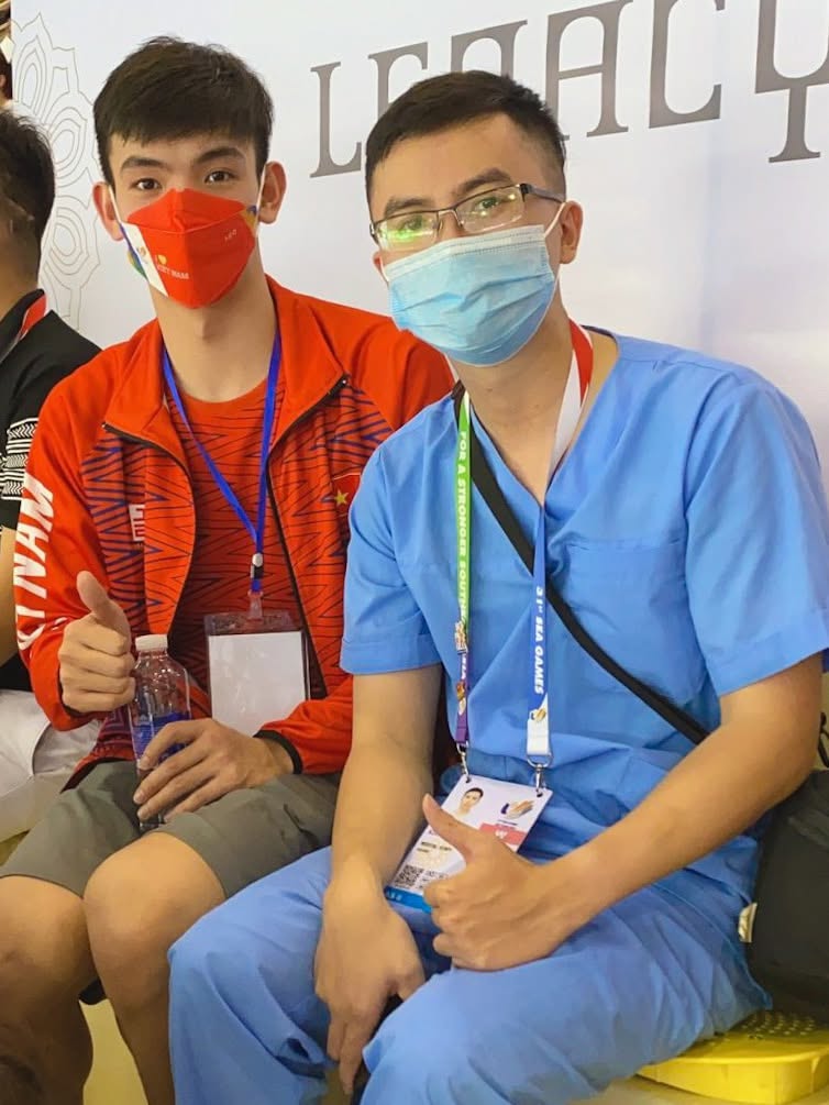 Bác sĩ Lê Trung Kiên trong bộ đồ y tế ngồi cạnh kình ngư Nguyễn Huy Hoàng tại khu vực thi đấu SEA Games 31