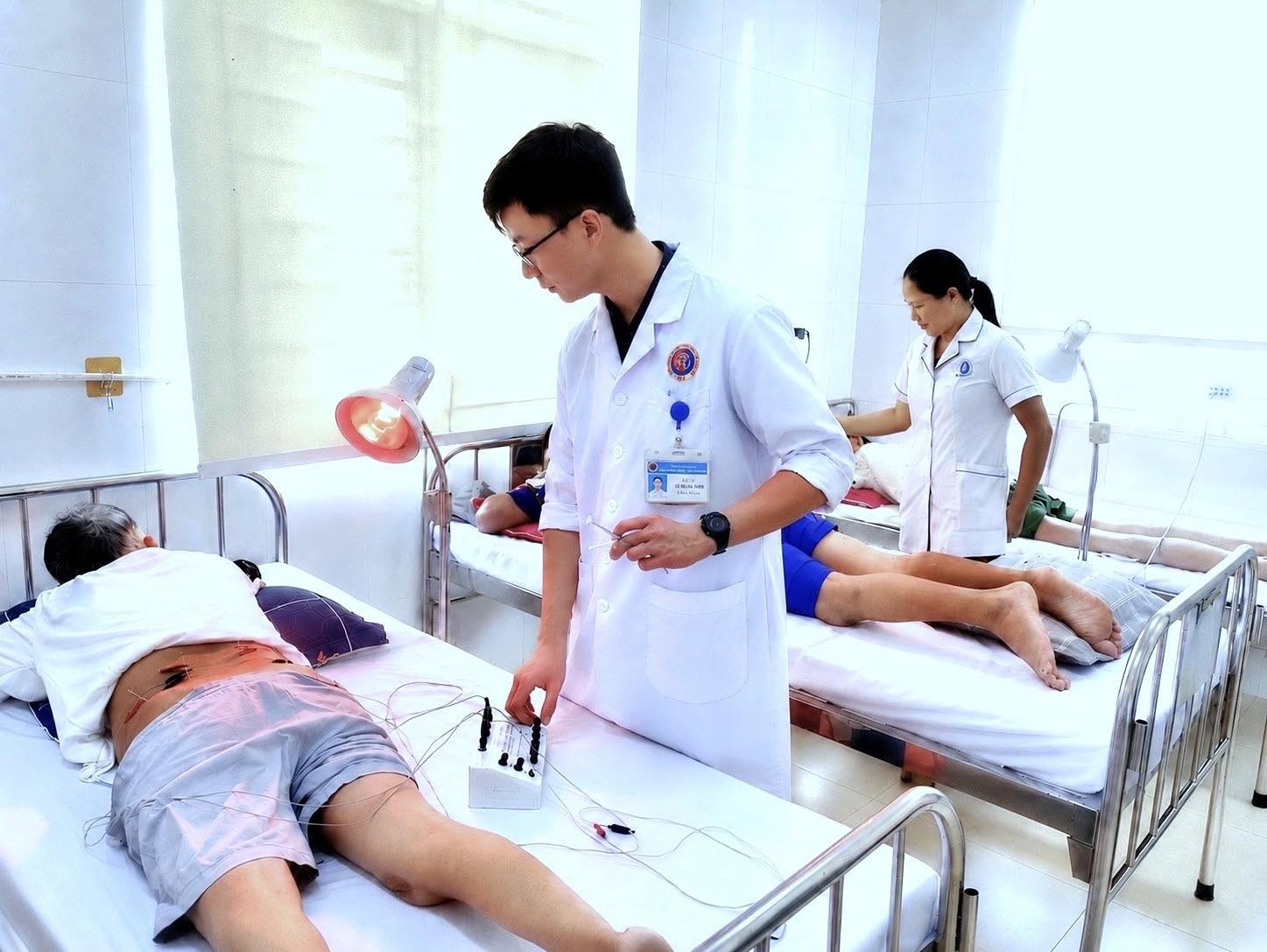 Bác sĩ Lê Trung Kiên điều chỉnh máy điện châm cho người bệnh tại phòng điều trị, kết hợp đèn hồng ngoại