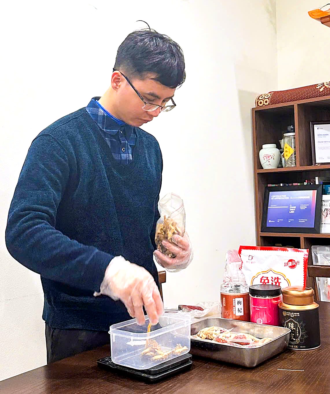 Bác sĩ Lê Trung Kiên đeo găng, cân dược liệu trên cân điện tử tại phòng khám